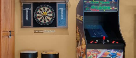 A room with a dartboard, a warning sign about video games, and an arcade machine.