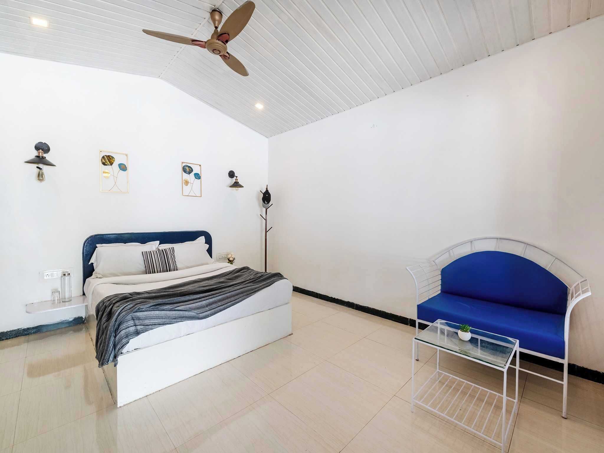 A bedroom with a bed, a ceiling fan, a blue sofa, and a small table with a plant.