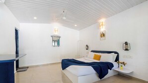 A bedroom with a bed, bedside table, wall-mounted lamp, and a small window. - Palette Santorini Pool Mountain View (Lonavala)