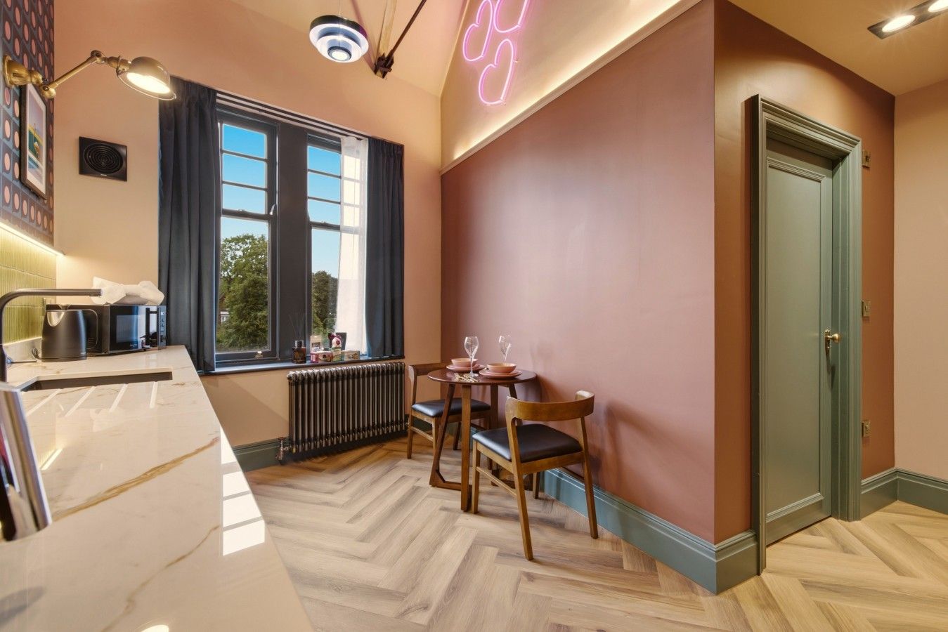 A modern kitchen with a dining area, a window with curtains, a radiator, and a door.