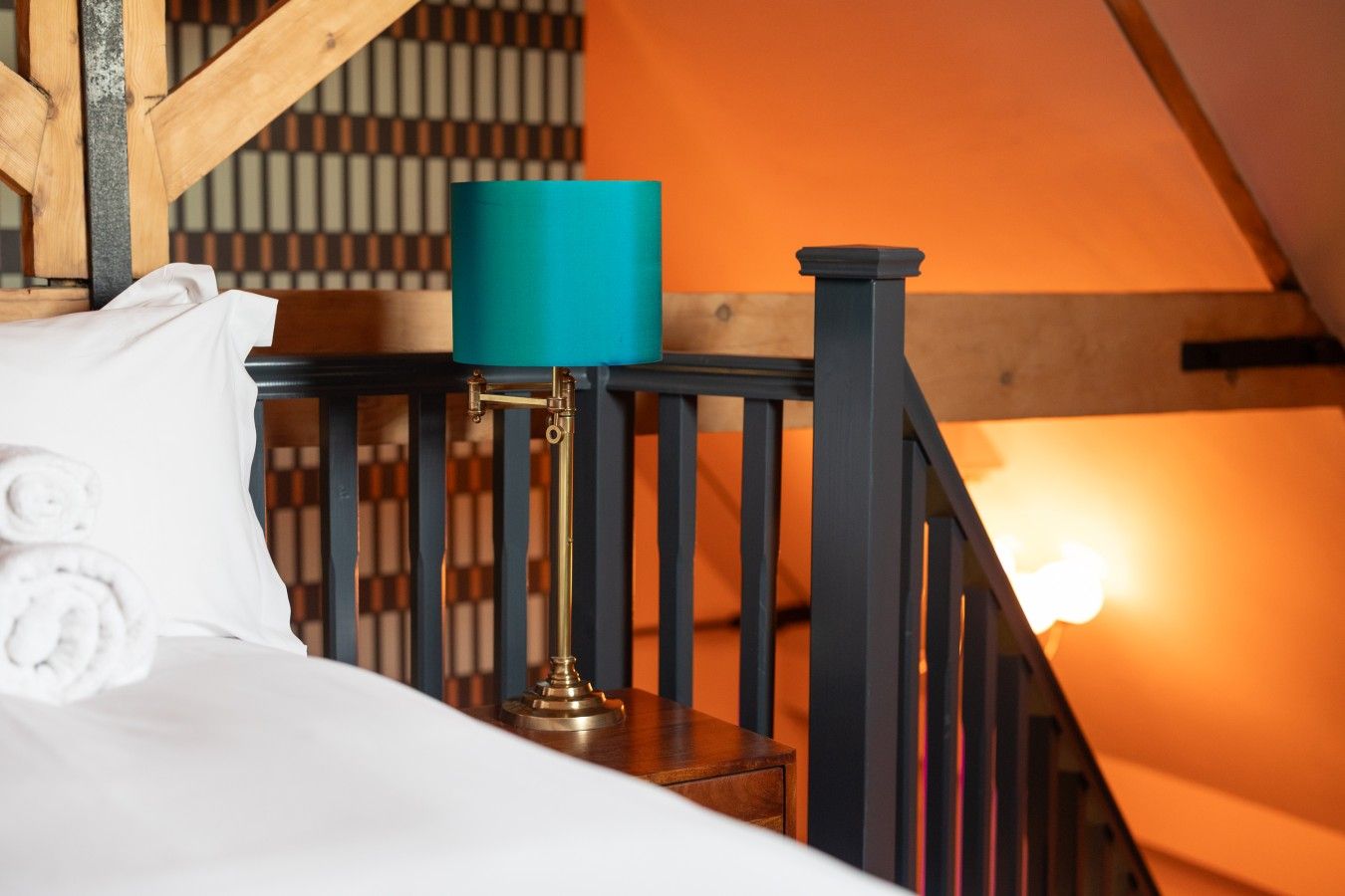 Een slaapkamer met een bed, een blauwgroene lamp en een houten trap.
