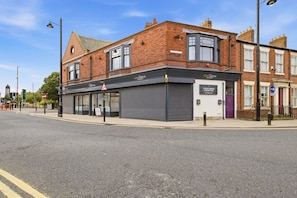 A street view with a brick building, a closed shop with a sign, and a blue directional sign. - The Loft - The Four Corner Collective (Sunderland)