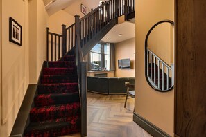 A staircase with a dark railing leading to a living area with a sofa and a television. - The Loft - The Four Corner Collective (Sunderland)