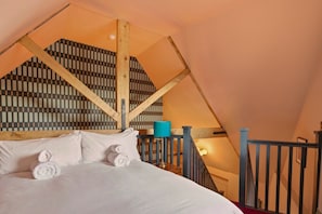 A bedroom with a sloped ceiling, a bed with white linens, a blue lamp, and a checkered wall pattern. - The Loft - The Four Corner Collective (Sunderland)