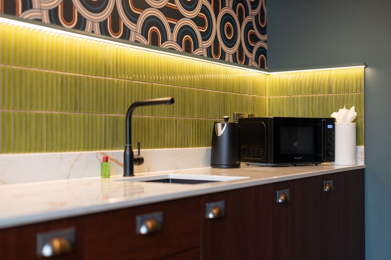 A modern kitchen with a sink, a kettle, a microwave, and a paper towel holder.