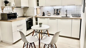 Une cuisine moderne avec des meubles blancs, un four à micro-ondes, une cuisinière et un coin repas comprenant deux chaises blanches et une petite table.