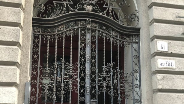 Un portail en fer forgé orné de motifs complexes, une plaque de numéro de maison et la façade d’un bâtiment avec des éléments en pierre.