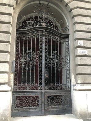 Un portail en fer forgé orné de motifs complexes, une plaque de numéro de maison et la façade d’un bâtiment avec des éléments en pierre.
