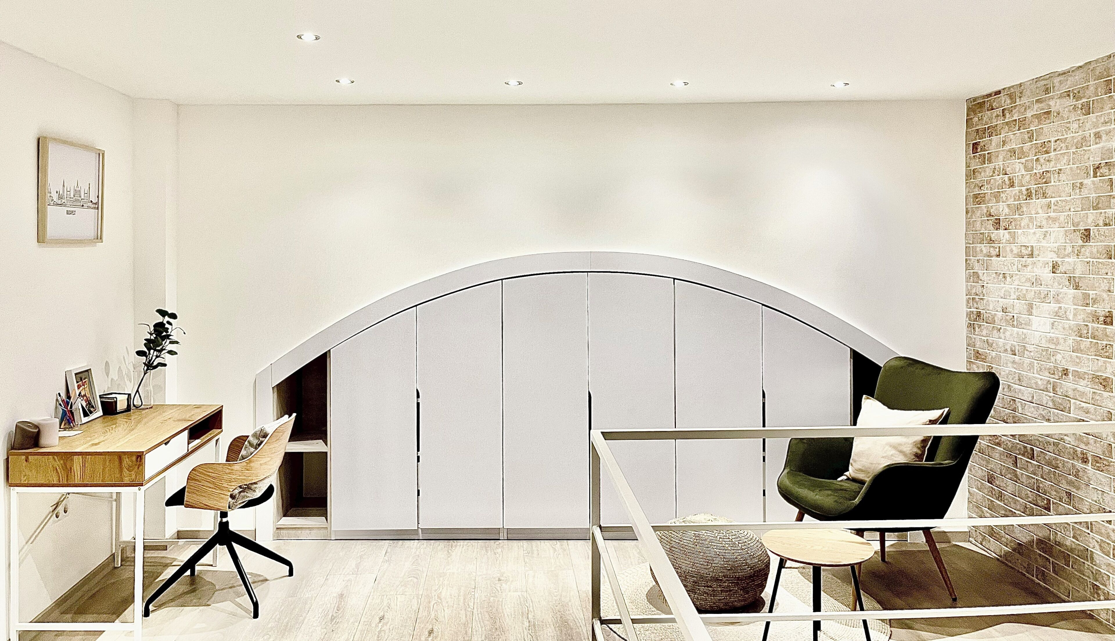 A modern room with a curved white wardrobe, a desk with a chair, a green armchair, and a glass partition.