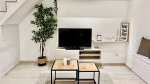 Un salon moderne doté d’un téléviseur à écran plat, d’une plante en pot, d’une petite table et d’étagères intégrées où sont disposés des objets décoratifs.