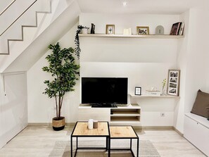 Ein modernes Wohnzimmer mit Flachbildfernseher, einem Blumentopf, einem kleinen Tisch und eingebauten Regalen mit Dekoration.