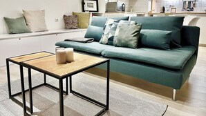 Un salon moderne avec un canapé vert, une petite table en bois et un coin cuisine à l’arrière-plan.