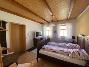 A bedroom with a wooden ceiling, a bed with patterned bedding, a television on a dresser, and a window with curtains.