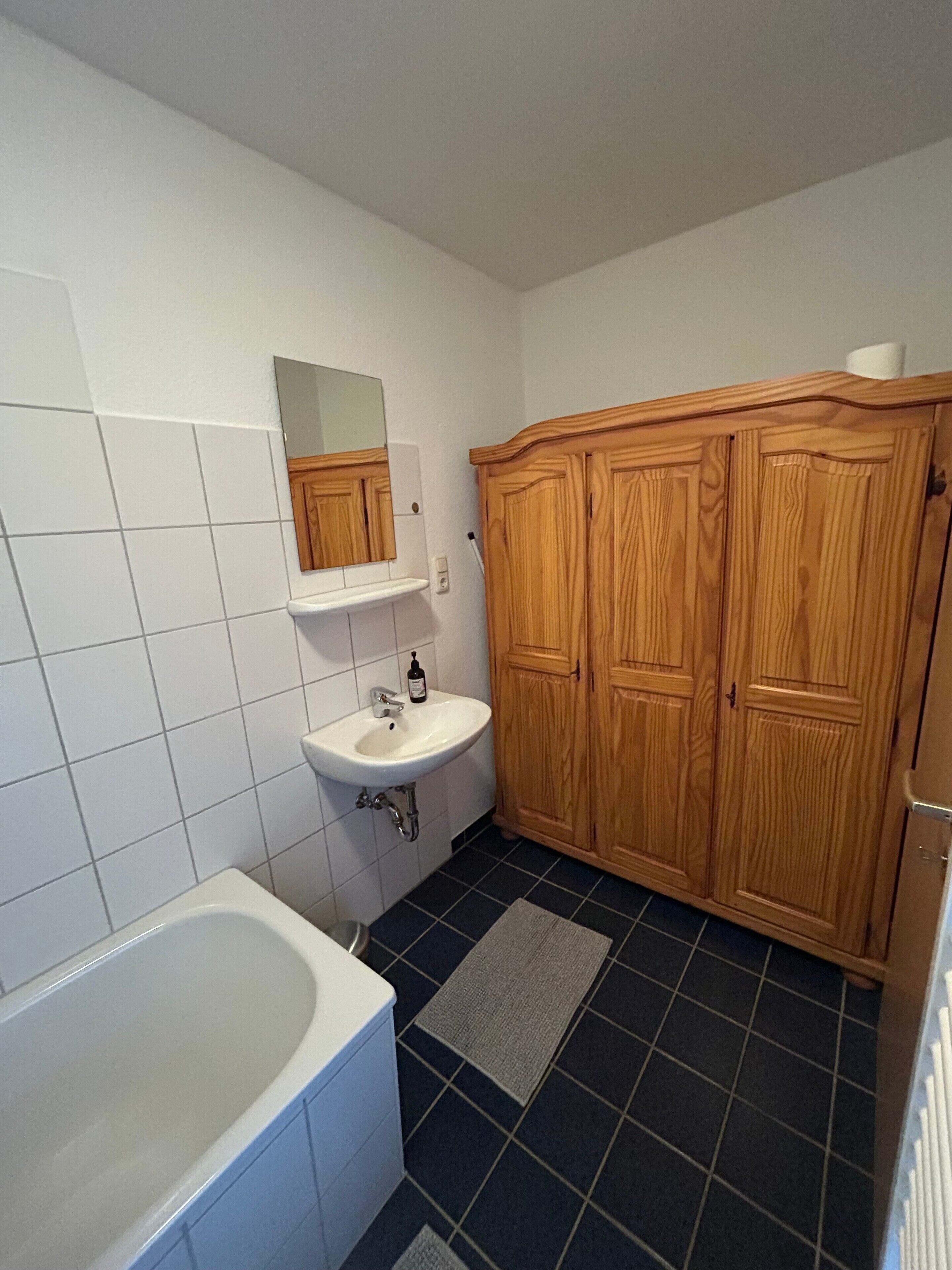Ein Badezimmer mit Waschbecken, Spiegel, Holzschrank und Badewanne.