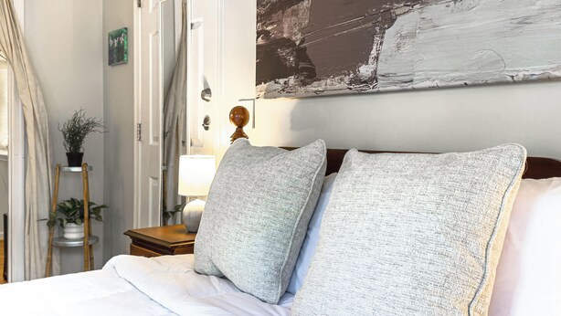 A bedroom with a bed, pillows, a nightstand, a lamp, a wall painting, and a door. - The Guest Suite | Walk to IX Park, Downtown Cville (Charlottesville)