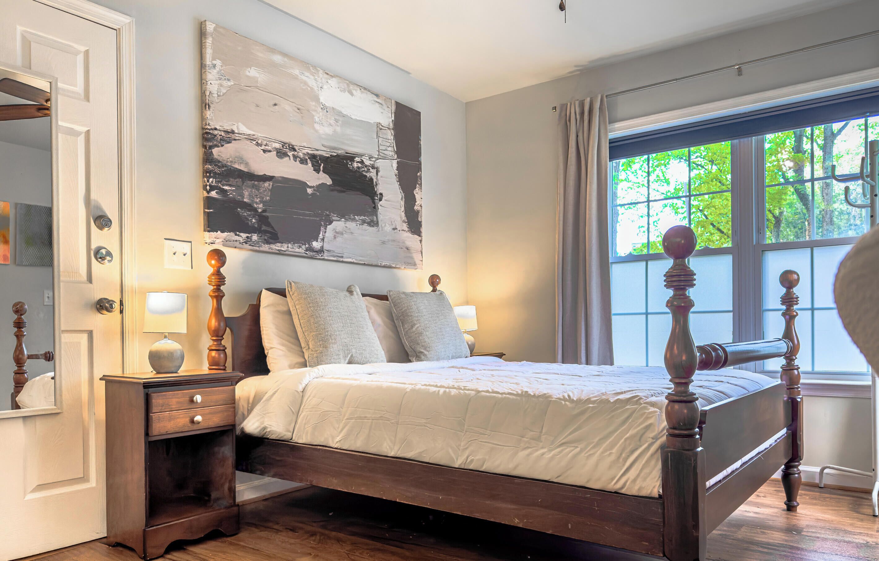A bedroom with a wooden bed, a nightstand, a wall-mounted lamp, and a large abstract painting.