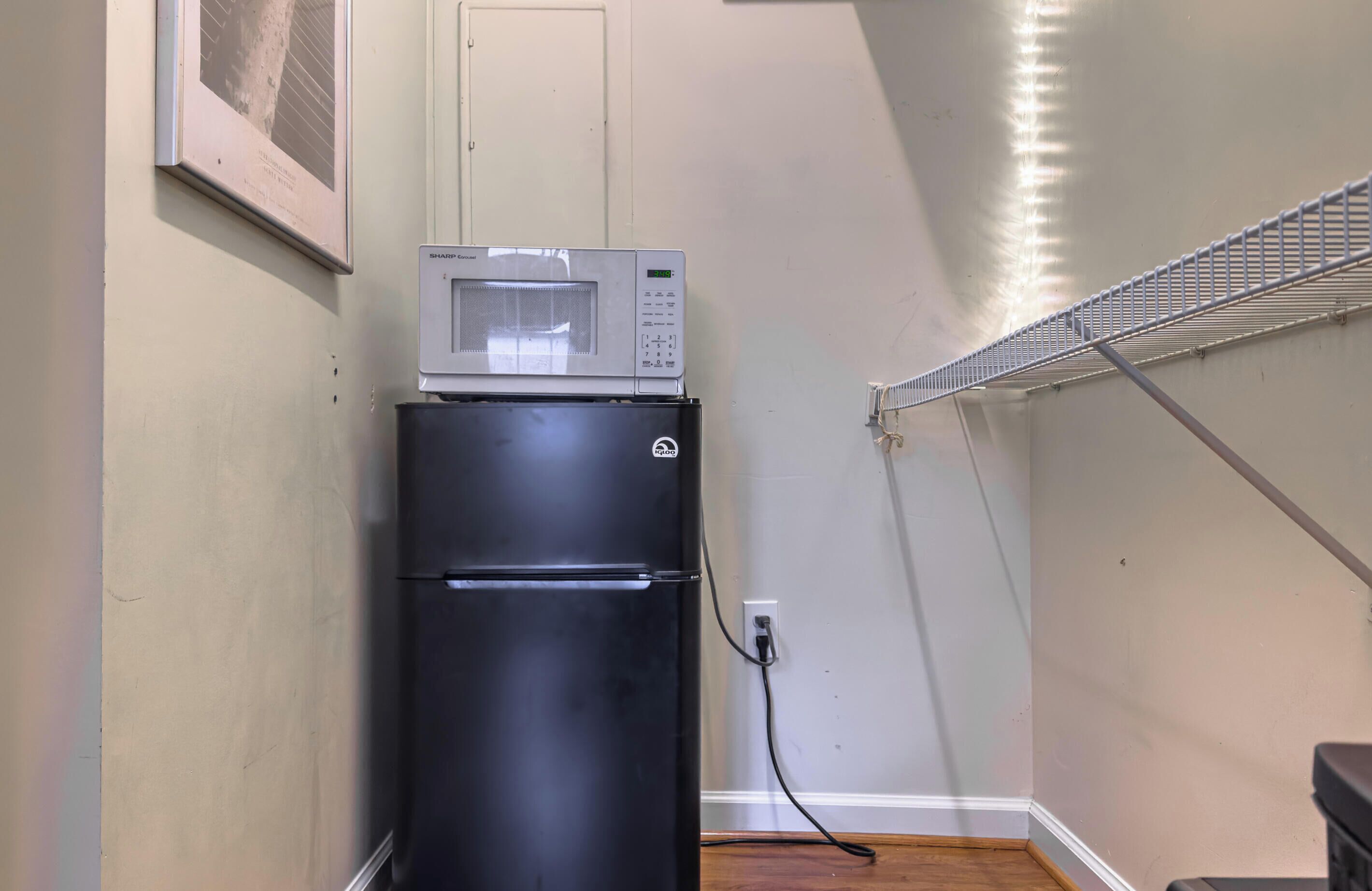 A compact kitchenette with a black refrigerator, a microwave, and a power outlet on the wall.