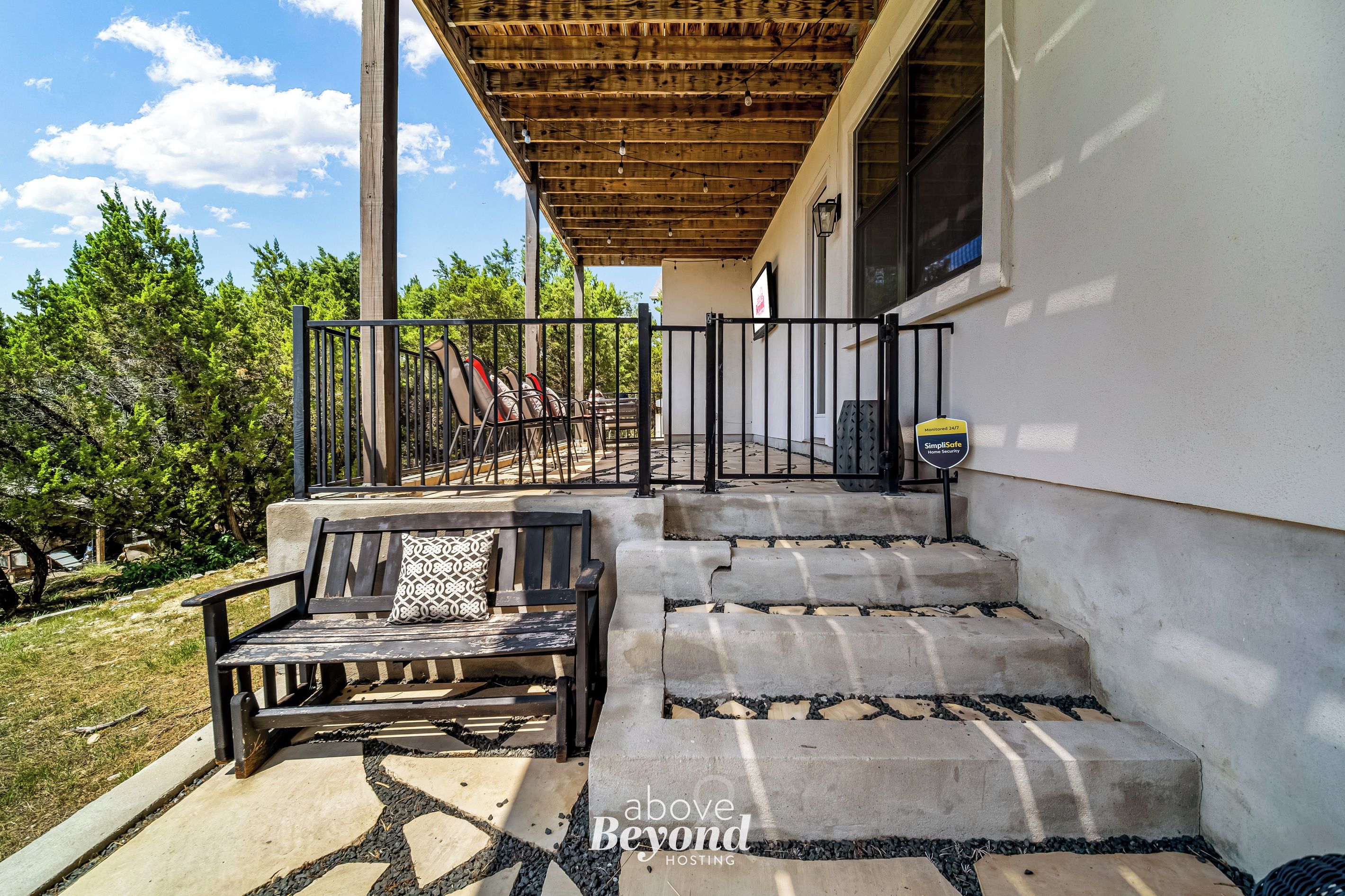 A covered outdoor seating area with a bench, steps leading to a door, and a security sign.