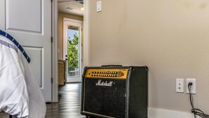 A room with a Marshall amplifier, a door leading to a balcony, and a white wall with a power outlet. - Creamy Cliffside Modern Casa (Lago Vista)