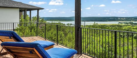A balcony with two lounge chairs and a view of a lake and hills.
