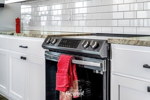 A kitchen with white cabinets, a stainless steel oven, and a red towel hanging on the oven handle. - Creamy Cliffside Modern Casa (Lago Vista)
