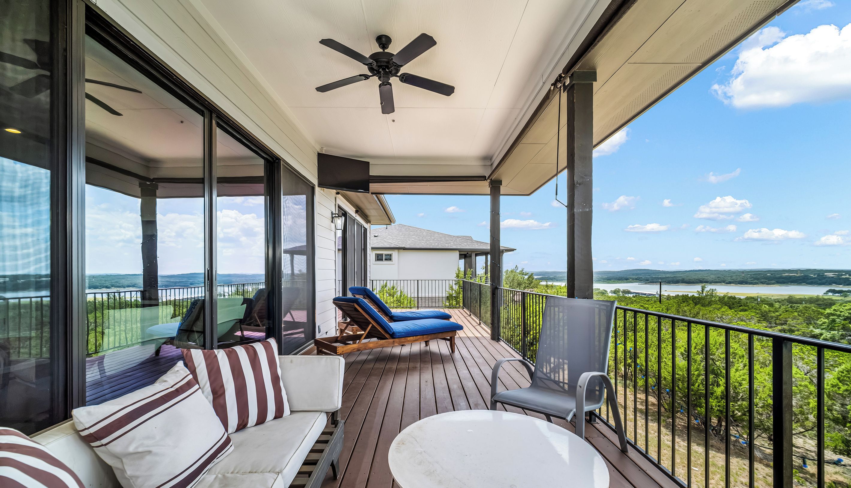 A covered outdoor deck with a ceiling fan, a sofa with striped cushions, and a view of a lake and hills.