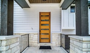 A wooden door with horizontal slats, a stone wall, and a black metal railing.