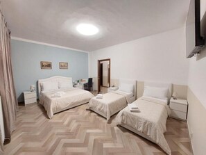 Habitación de hotel con tres camas, un escritorio, una silla y un espejo.