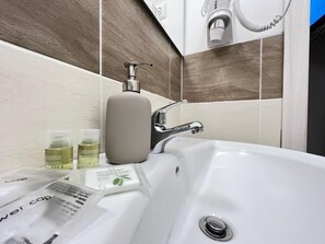 Un baño con un lavamanos blanco, un dispensador de jabón y una botella de aceite de oliva.