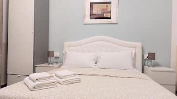 Una cama bien tendida con una colcha estampada, dos lámparas de noche, un cuadro enmarcado en la pared y un armario a la izquierda.