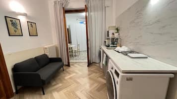 Un ambiente compatto con divano, lavatrice, angolo cottura e tavolo da pranzo.