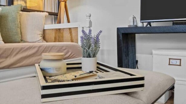 Ein ordentlich eingerichtetes Wohnzimmer mit einer Couch, einem Couchtisch mit Tablett, einer Lampe und einem Fernseher.