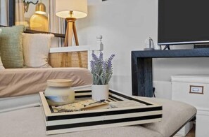 Ein ordentlich eingerichtetes Wohnzimmer mit einer Couch, einem Couchtisch mit Tablett, einer Lampe und einem Fernseher.