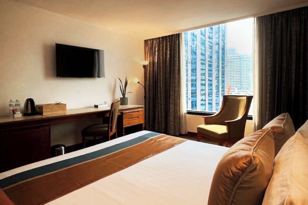 Een hotelkamer met een bed, bureau, stoel, televisie en een raam met gordijnen.