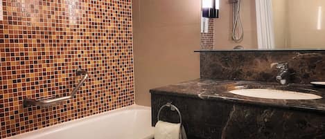 A bathroom with a mosaic tile wall, a bathtub, a sink with a marble countertop, and a shower area.