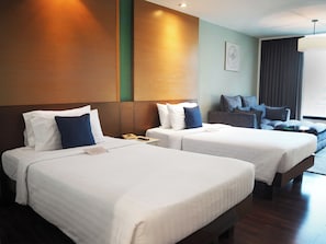 A hotel room with two beds, a sofa, a desk, and a large window. - Awtan Sukhumvit (Bangkok)