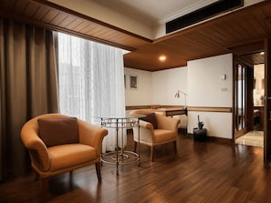 A hotel room with a wooden floor, two leather armchairs, a small round table, and a large window with curtains. - Awtan Sukhumvit (Bangkok)