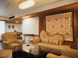 A living room with a glass coffee table, two armchairs, a sofa, and a patterned tapestry on the wall. - Awtan Sukhumvit (Bangkok)
