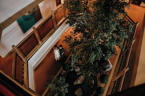 A multi-level indoor space with a central staircase, wooden railings, and a large artificial tree. - Awtan Sukhumvit (Bangkok)