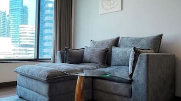 A modern living room with a grey sectional sofa, a wooden coffee table, and a city view through large windows.