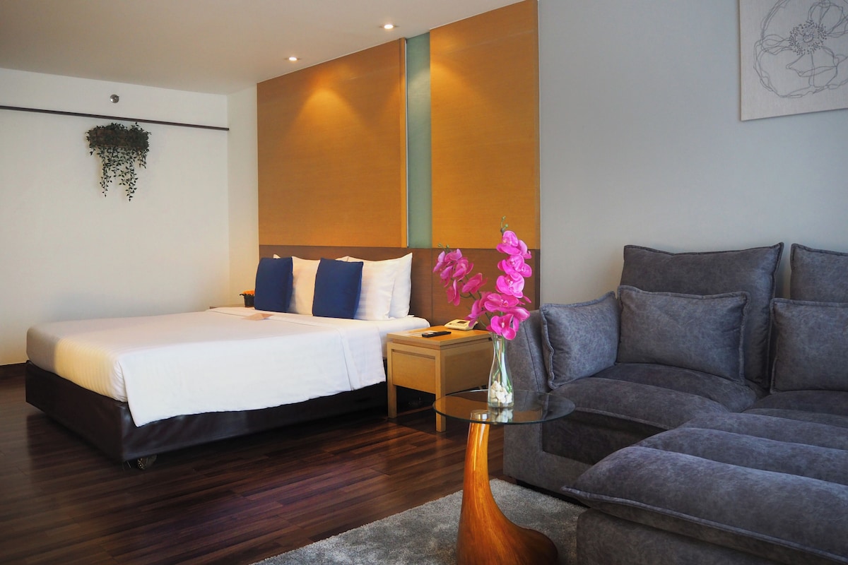 Een hotelkamer met een bed, een slaapbank, een nachtkastje en een vaas met bloemen.