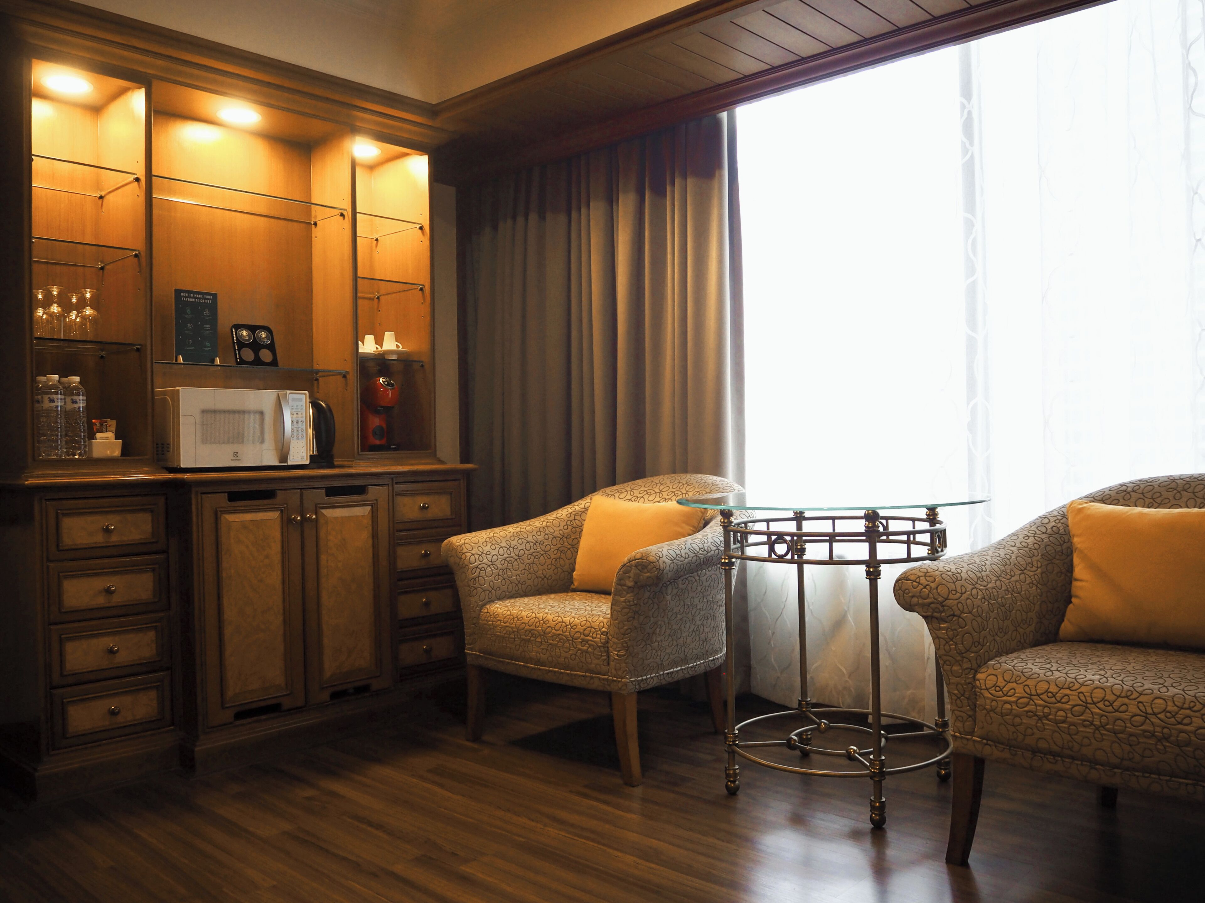 A hotel room with a wooden cabinet, a microwave, a coffee maker, and two patterned armchairs.