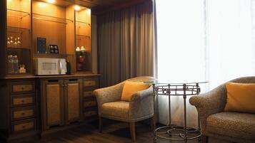 A hotel room with a wooden cabinet, a microwave, a coffee maker, and two patterned armchairs.
