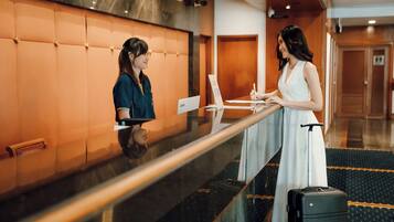 Two individuals at a hotel reception desk with a luggage trolley and a Lenovo sign.