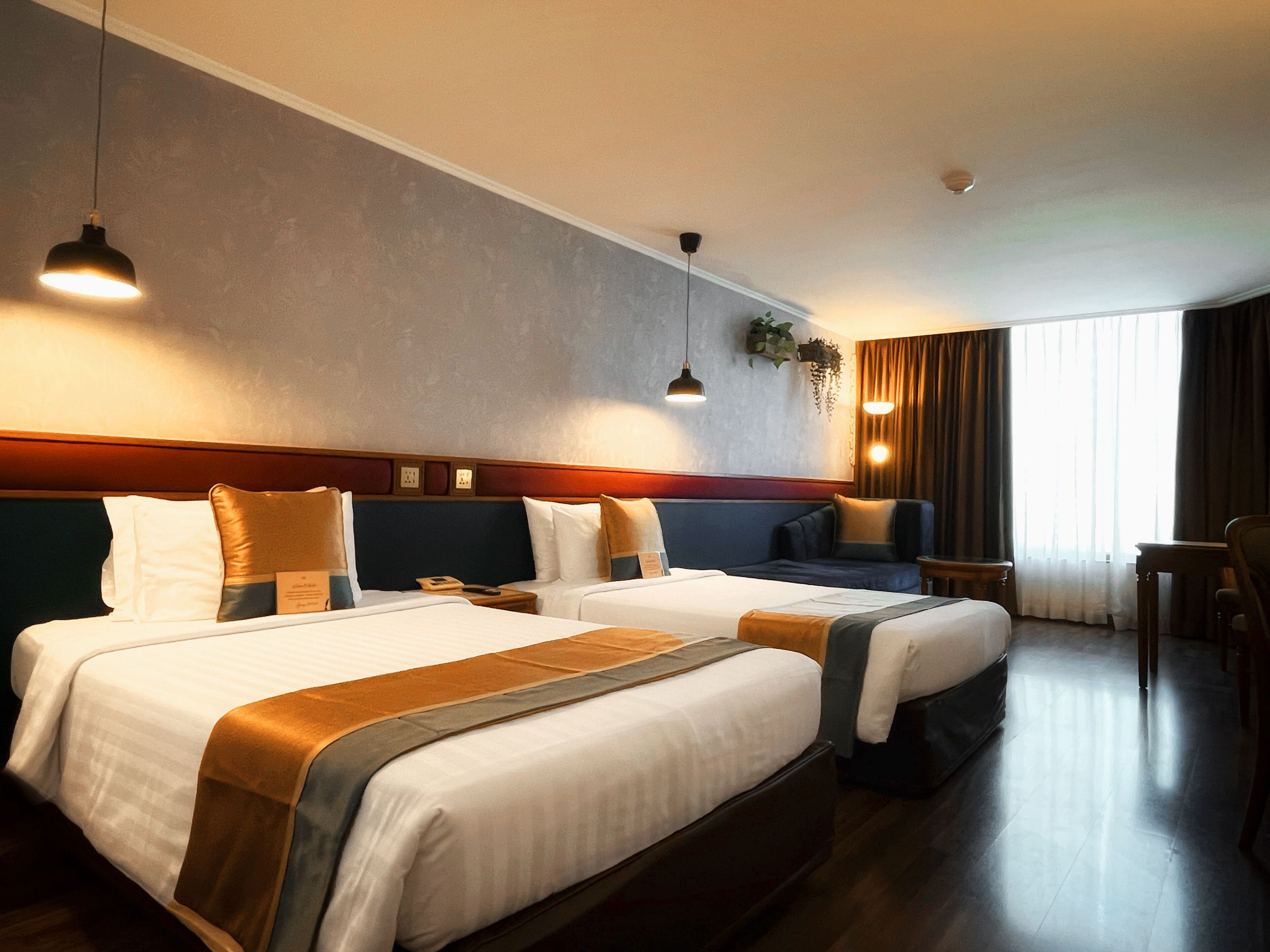 A hotel room with two beds, a sofa, a desk, and a large window with curtains.
