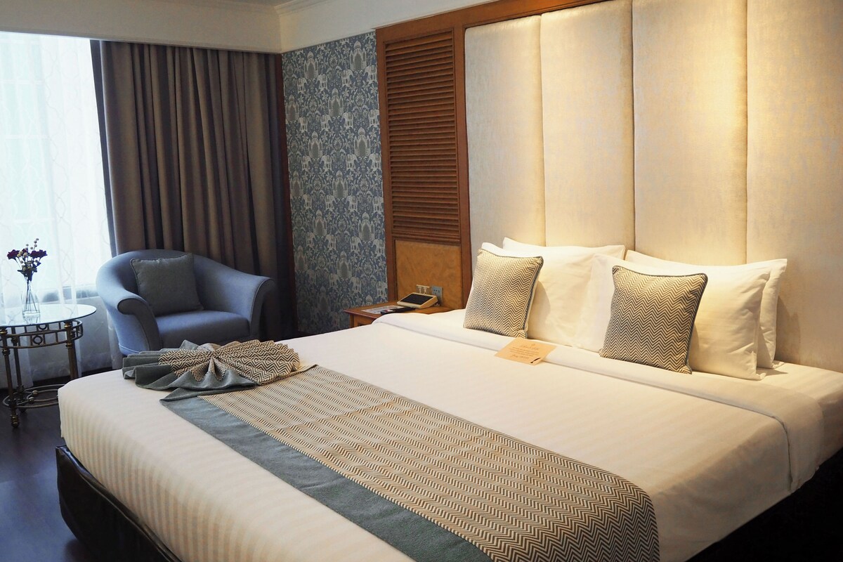 Een hotelkamer met een groot bed, een stoel, een bijzettafeltje en een raam met gordijnen.