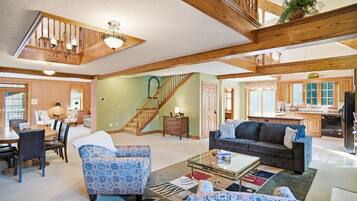 A spacious living area with a staircase, wooden beams, a dining set, and a kitchen in the background.