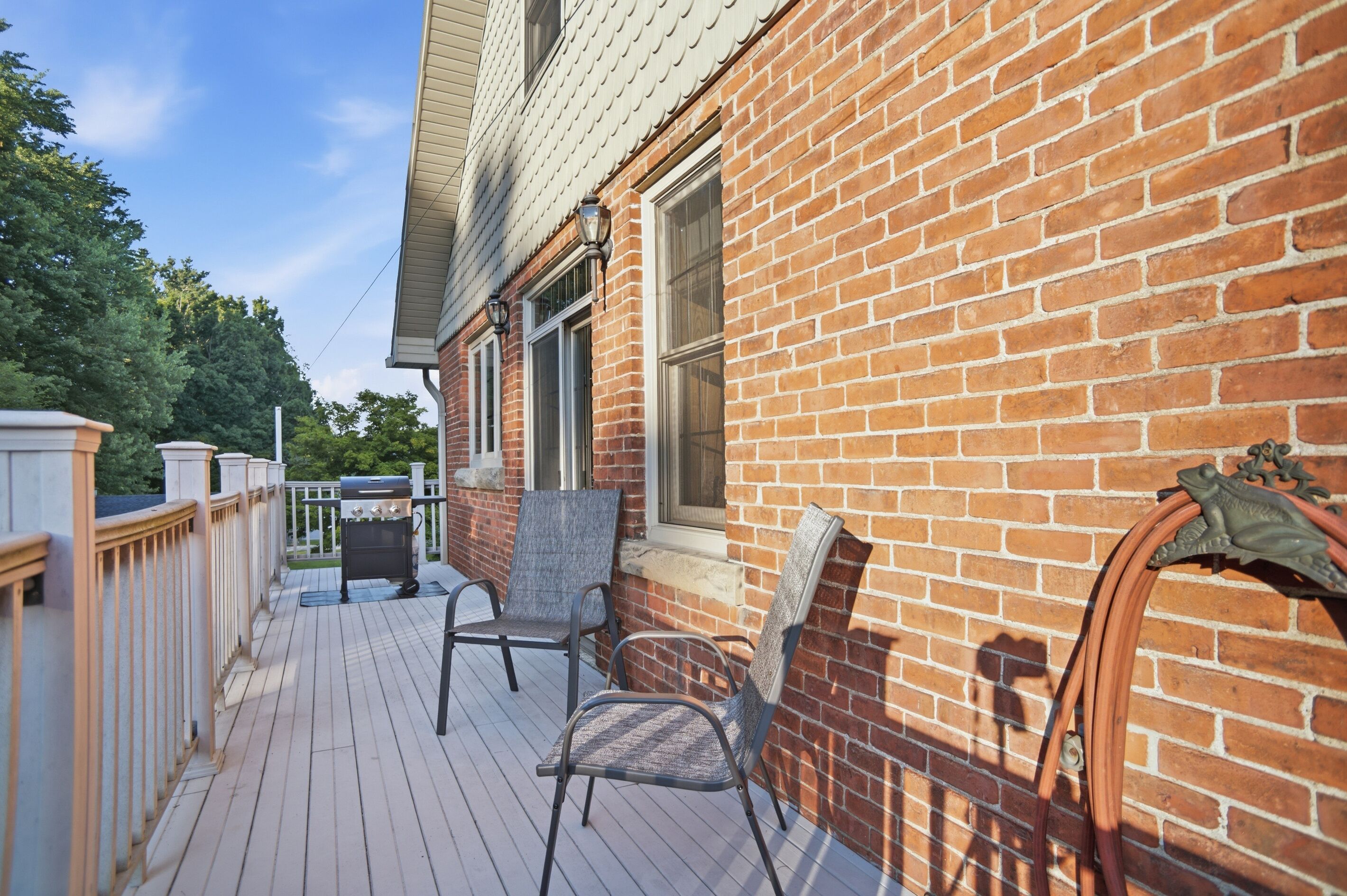 A wooden deck with outdoor seating, a brick wall, and a window.