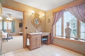 A bathroom with a vanity, a mirror, a window with curtains, and a ceiling fan.