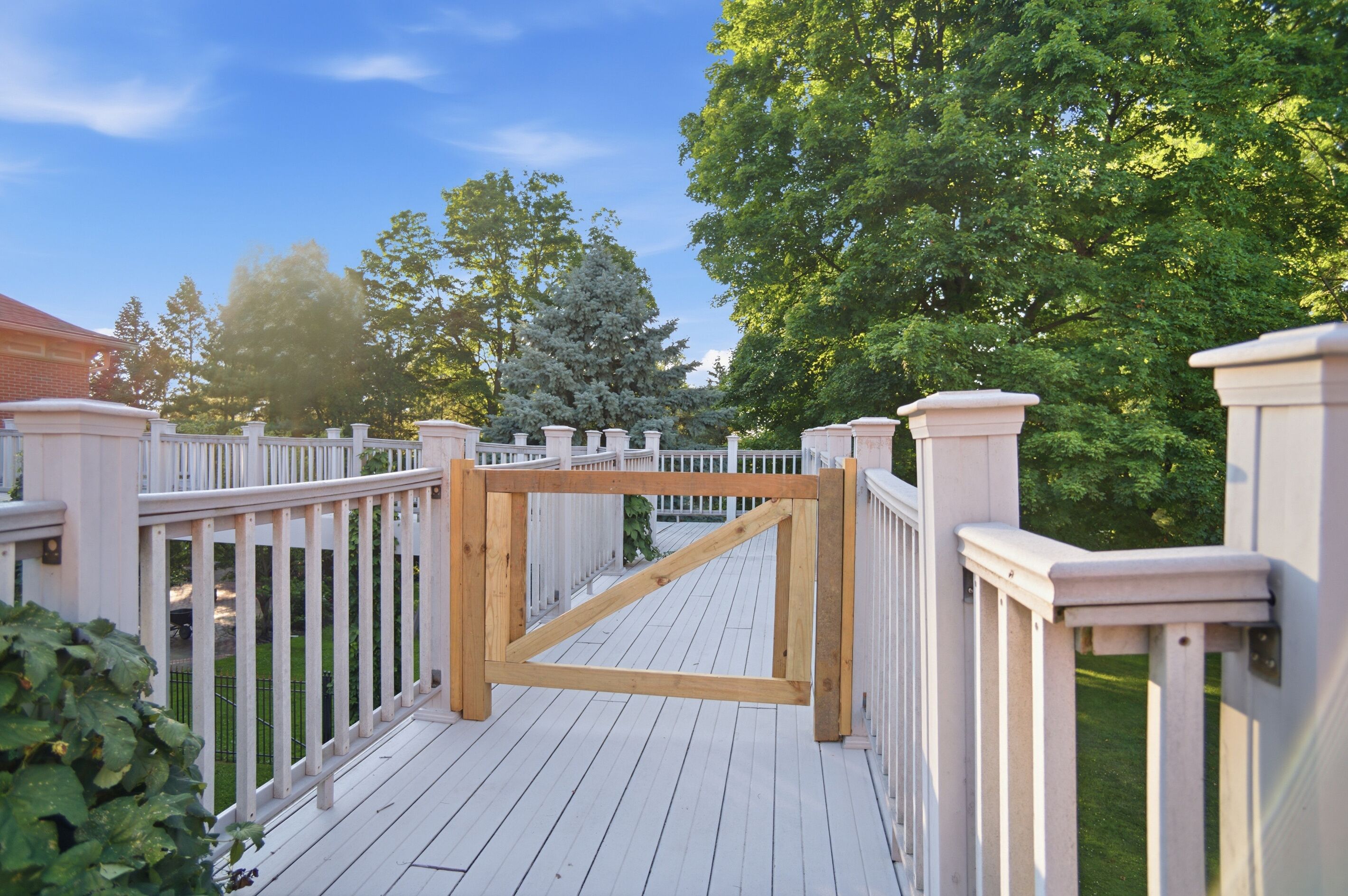 A wooden deck with white railings, surrounded by trees and a clear sky.